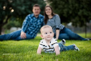 baby poses in grass with parents blurred in background