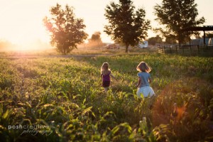 Little girls run in corn field together at sunrise